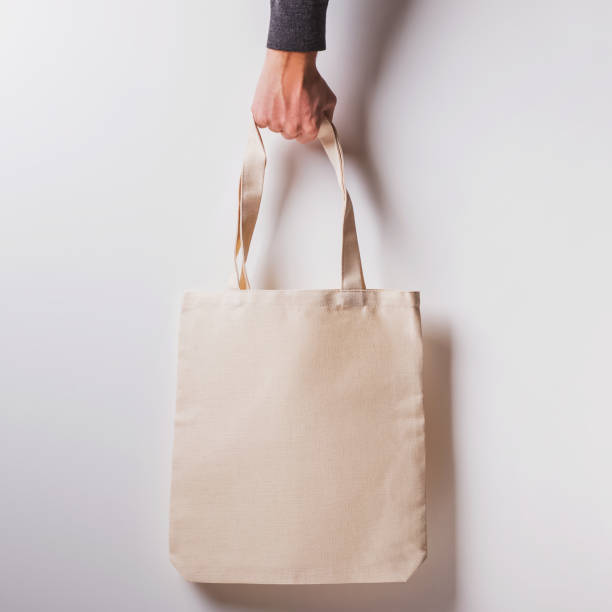 istock Man's hand holds blank cotton eco tote bag over the white wall 1219352255