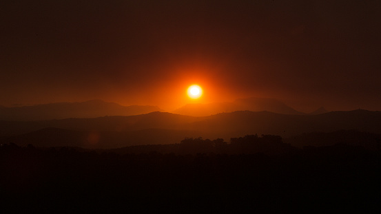 Red African sunrise glow during field fire season over rolling hills towards Table Mountain Cape Town