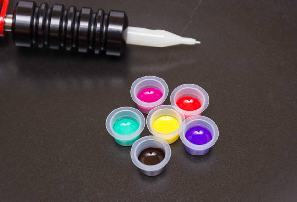 istock Rotary tattoo machine and disposable plastic jars with colored paints on a black background. Side view 1219355621