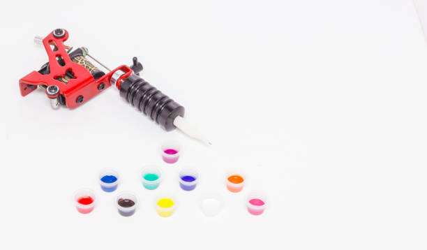 istock Induction tattoo machine and color paints in disposable plastic jars on a white background. Free space for text. Tattoo equipment. Side view. 1219355645