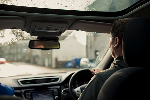 Over shoulder view of a mature man driving a car. The man is in focus while the view out of the windscreen is falling out of focus.