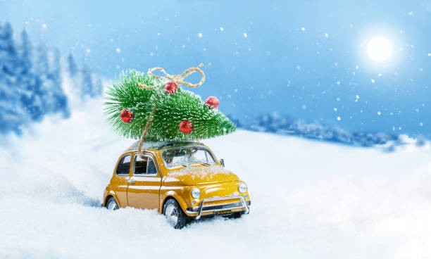雪の多い冬の森の屋根にクリスマスツリーを運ぶレトロなおもちゃの車。クリスマスの背景。休日カード。スペースをコピーします。 - gift snow yellow christmas ストックフォトと画像