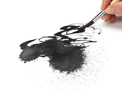 Hand with paint brush and Black ink blot on white background.
