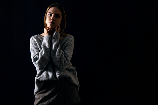 young pretty girl in a gray sweater with a calm pensive expression on a dark background, low key, copy space