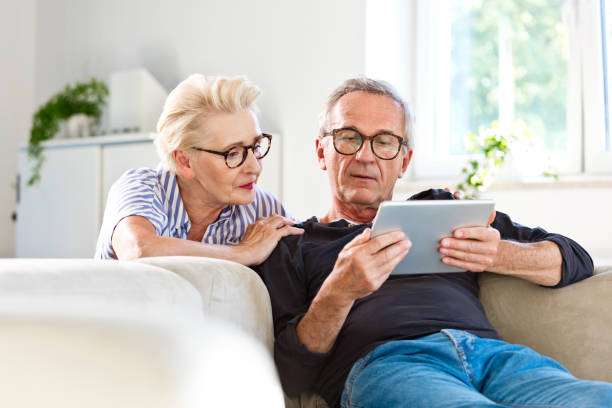 coppia senior che guarda il tablet digitale insieme a casa - discussion couple senior adult inside of foto e immagini stock