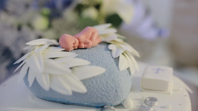 Decorated cake for newborn baby on table with baby doll decorated on top. Cake for christening event