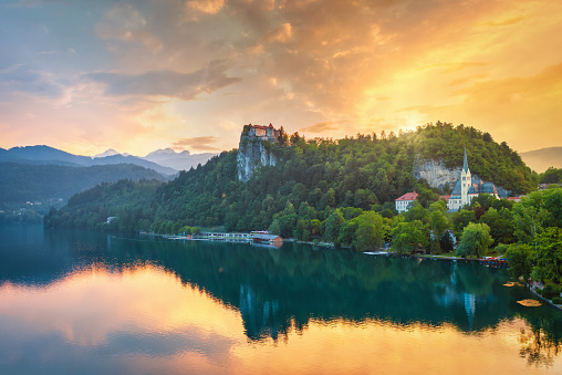 Colorful dramatic Sunset over Lake Bled. Beautiful view over famous Lake Bled with St. Martin's Parish Church and Bled Castle on Clifftop together with the Lake Waterfront Promenade. Lake Bled Hill Range reflecting in the tranquil lake water. Lake Bled, Slovenia, Central Europe
