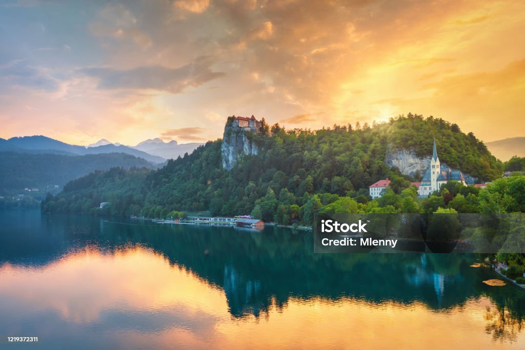 Dramatic Sunset over Lake Bled in Slovenia Colorful dramatic Sunset over Lake Bled. Beautiful view over famous Lake Bled with St. Martin's Parish Church and Bled Castle on Clifftop together with the Lake Waterfront Promenade. Lake Bled Hill Range reflecting in the tranquil lake water. Lake Bled, Slovenia, Central Europe Slovenia Stock Photo