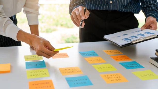 istock Business people arranging sticky notes commenting and brainstorming on work priorities colleague in a modern co-working space 1219374315