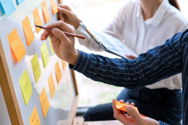istock Business people arranging sticky notes commenting and brainstorming on work priorities colleague in a modern co-working space 1219374422