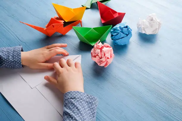 The child at the table makes origami from colored paper.