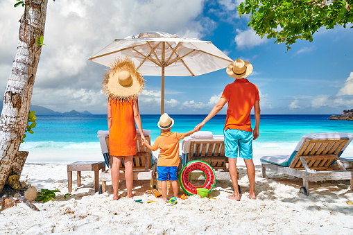 Family on beautiful Petite Anse beach, young couple with three year old toddler boy. Summer vacation at Seychelles, Mahe.