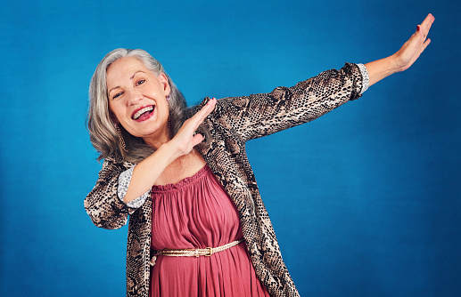 Portrait of a funky and cheerful senior woman dancing in studio against a blue background