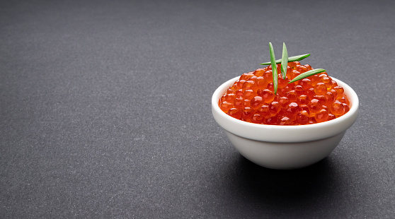 Red caviar in bowl close-up, salmon caviar on black stone background with copy space, seafood delicatessen