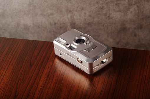 Vintage analog point and shoot film camera on wooden table with concrete textured wall as background