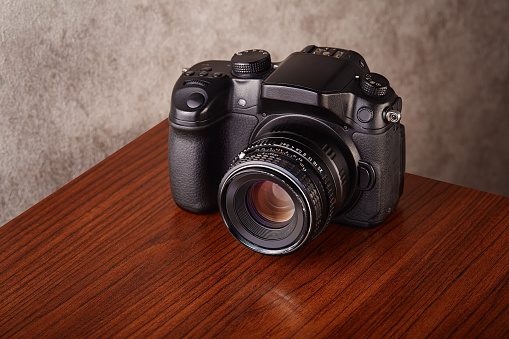 Digital mirrorless professional camera on wooden table with concrete wall as a background