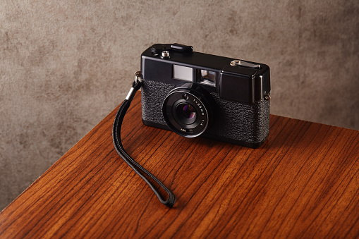 Vintage analog rangefinder film camera on wooden table with concrete textured wall as background