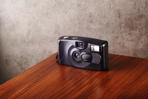 Vintage analog point and shoot film camera on wooden table with concrete textured wall as background