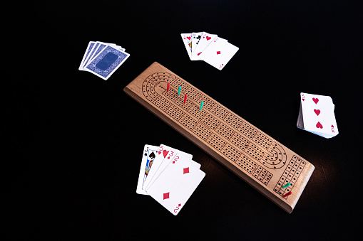 Cribbage board and cards set up on black table with pegs set up showing imminent victory.
