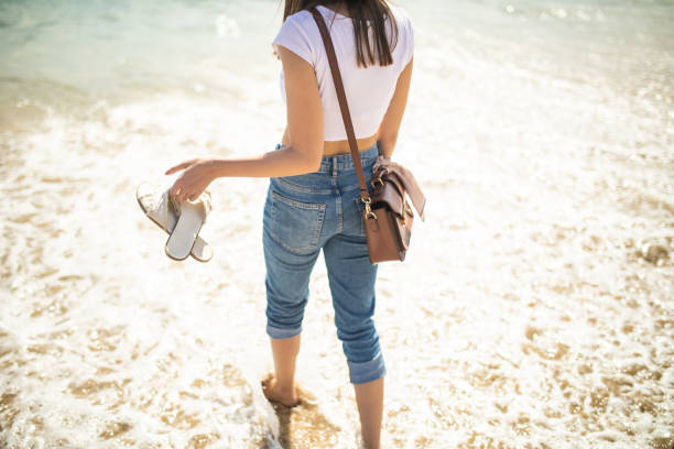 istock Young barefoot woman walking down seashore during beautiful day 1219386339