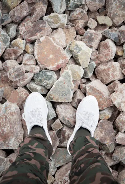 A man stands in the military pants and white sneakers on large stones