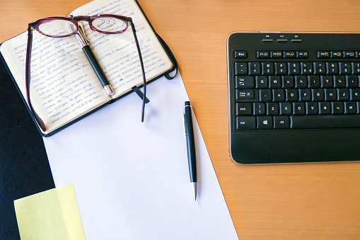 Desktop with blank paper, keyboard, eyeglasses, fountain pen, modern mechanical pencil and notebook