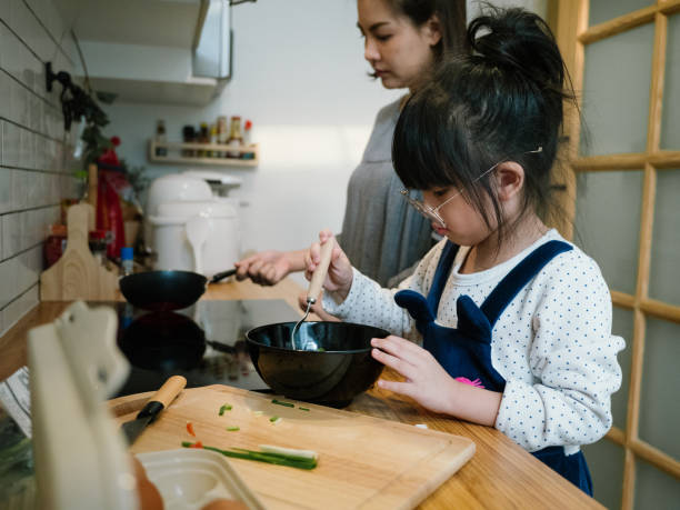 istock Millennial mother preparing breakfast at kitchen with her daugther's helping hand cooking omelet at home. 1219391087