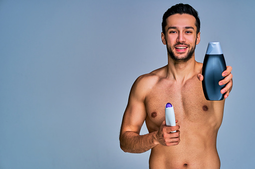 Happy tanned naked man with conditioner in hands gives one away