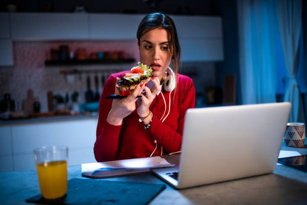istock Young woman working from home late at night. She is having a sandwich while using a laptop 1219393093