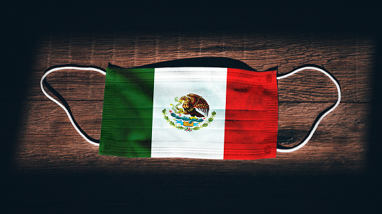Mexico National Flag at medical, surgical, protection mask on black wooden background. Coronavirus Covid\