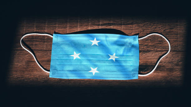 micronesia, federated states of national flag at medical, surgical, protection mask on black wooden background. coronavirus covid"u201319, prevent infection, illness or flu. state of emergency, lockdown... - federated imagens e fotografias de stock