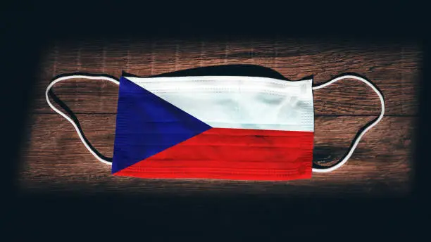 Photo of Czech Republic National Flag at medical, surgical, protection mask on black wooden background. Coronavirus Covid