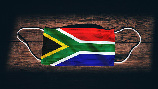 South Africa National Flag at medical, surgical, protection mask on black wooden background. Coronavirus Covid\
