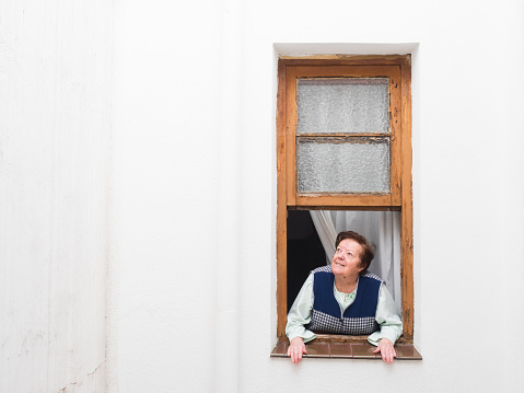 A senior woman peeps through window in  quarantine Coronavirus with acooking pot