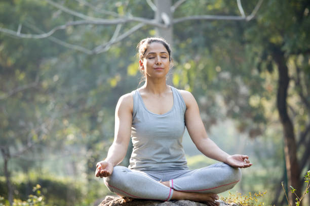 istock Woman practicing yoga in lotus position at park 1219401176