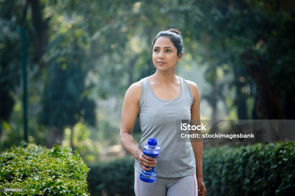 Fit woman with dumbbell shape water bottle at park Fit woman running in sportswear with dumbbell shape water bottle at park Walking Stock Photo