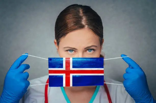 Coronavirus in Iceland Female Doctor Portrait hold protect Face surgical medical mask with Iceland National Flag. Illness, Virus Covid-19 in Iceland, concept photo