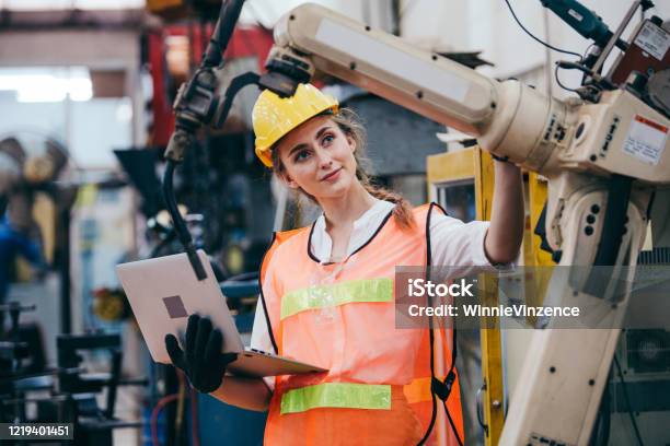Female Industrial Engineer Or Technician Worker In Hard Helmet And Uniform Using Laptop Checking On Robotic Arm Machine Woman Work Hard In Heavy Technology Invention Industry Manufacturing Factory Stock Photo - Download Image Now