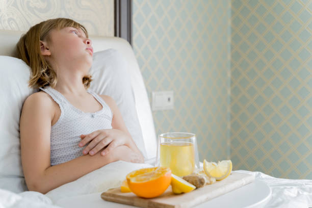 Little sick girl in bed with cup of antipyretic drugs for colds,flu.Tea with citrus vitamin C,ginger root,lemon,orange.Wooden tray. Home self-treatment.Medical quarantine covid-19 coronavirus therapy. pequeña niña enferma en la cama con taza de medicamentos antipiréticos para resfriados, gripe. té con vitamina c cítrica, raíz de jengibre, limón, naranja. bandeja de madera. autotratamiento en el hogar. cuarentena médica covid-19 terapia coronavir