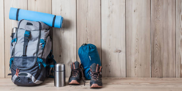 istock Camping equipment, shoes, a backpack and a thermos on a wood background 1219402418