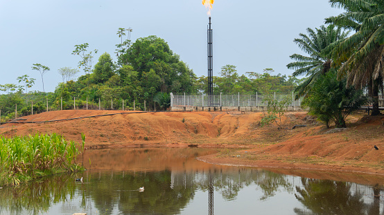 Front view of a production natural gas well tower burning gas on top near a lagoon in the middle of the jungle in Putumayo - Colombia