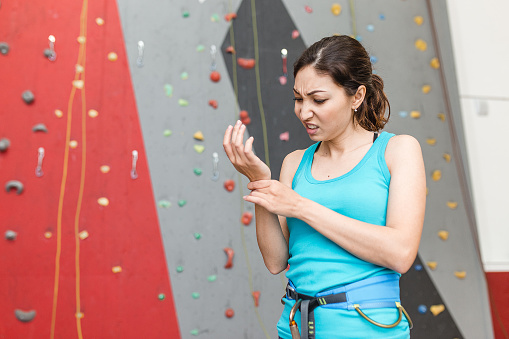 woman climber with the trauma and pain in the wrist on a background of climbing wall