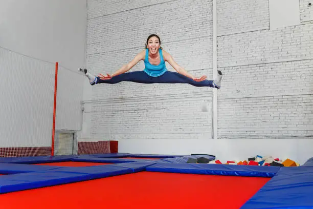 jumping young woman on the trampoline, white brick wall background