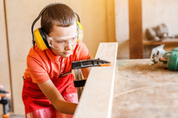 chłopiec w warsztacie samodzielnie uczy się pracować z drewnem w warsztacie stolarskim. koncepcja przydatnego hobby w dzieciństwie i uczenia się pracy ręcznej z rękami - manually zdjęcia i obrazy z banku zdjęć