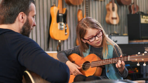 아빠는 딸에게 기타와 우쿨렐레를 가르치셨다. 집에서 기타를 배우는 어린 소녀. 닫아. 집에서 우쿨렐레 수업. 그녀의 아버지로부터 기타를 배우는 아이 - guitar child music learning 뉴스 사진 이미지