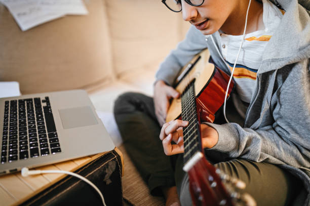 istock Teenage boy learning to play guitar watching online tutorial 1219408701