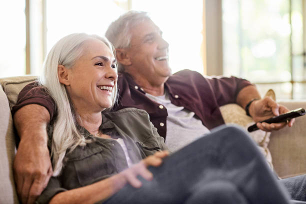 Happy couple watching TV at home Cheerful mature woman and man watching TV. Happy couple is spending weekend together. They are sitting on sofa at home. 55 59 years photos stock pictures, royalty-free photos & images