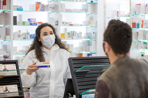 Female pharmacist wearing a surgical mask tells the male patient who wears a surgical mask how to use his medicine