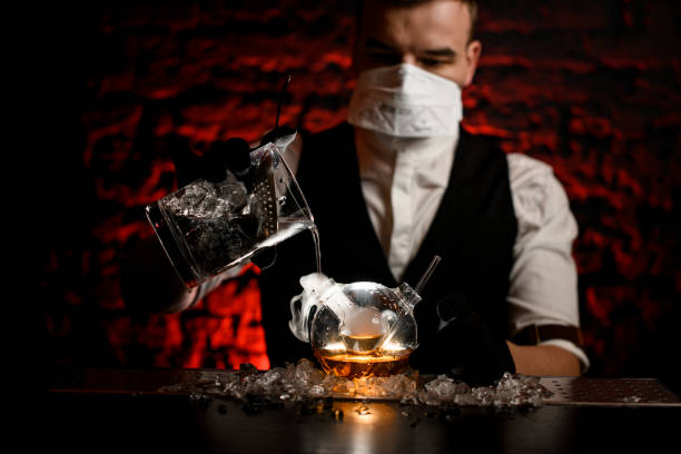 istock bartender in mask with black gloves pours drink into special flask 1219410432