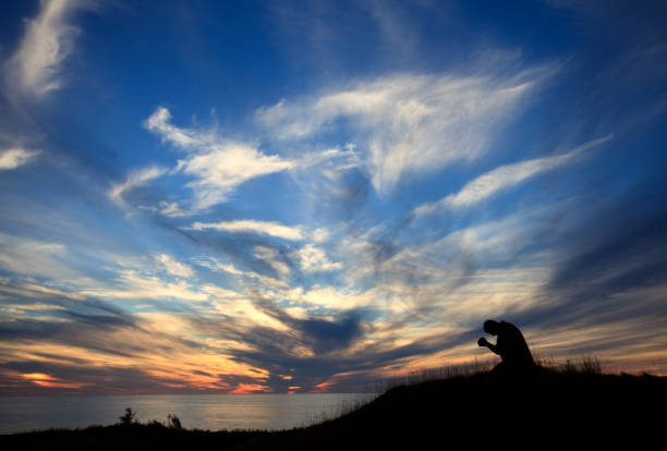 silhouette des menschen auf seinen knien im gebet durch den ozean gegen schönen sonnenuntergang himmel - praying men god kneeling stock-fotos und bilder